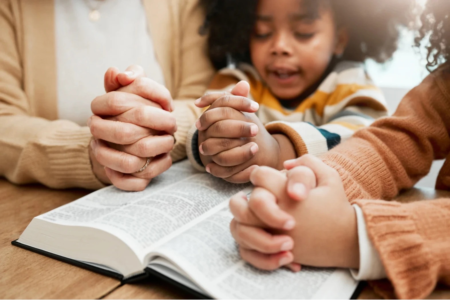 A mother and her children with hands folded in prayer over an open Bible